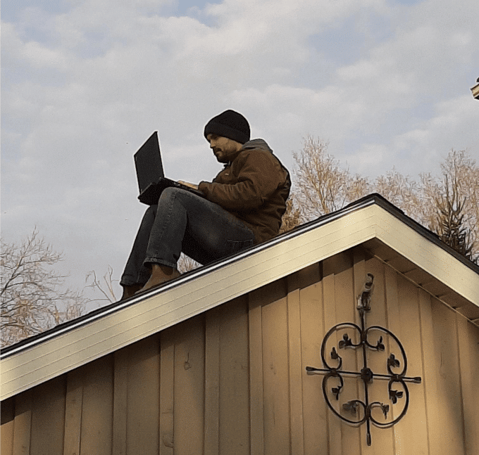 Sean sits on the roof of his home with a laptop computer.